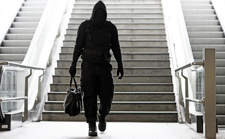 Hooded Lone wolf Man wearing black carrying bag in urban underground public transport setting