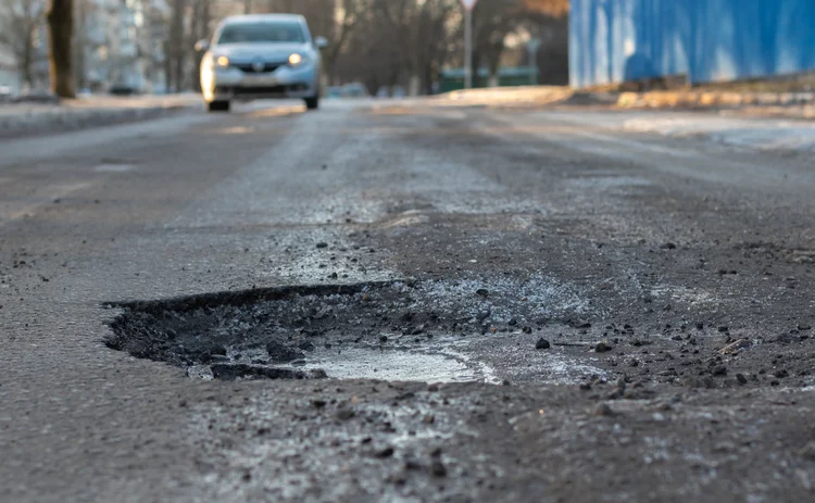 A pothole in the road and a car in the background that is moving towards this pothole