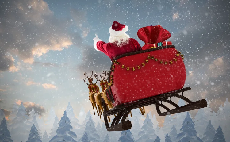 Santa Claus riding on sled with gift box against snow falling on fir tree forest