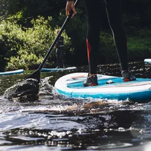 Close up of somones lower body as they paddleboard in a lake. There are other people around them.